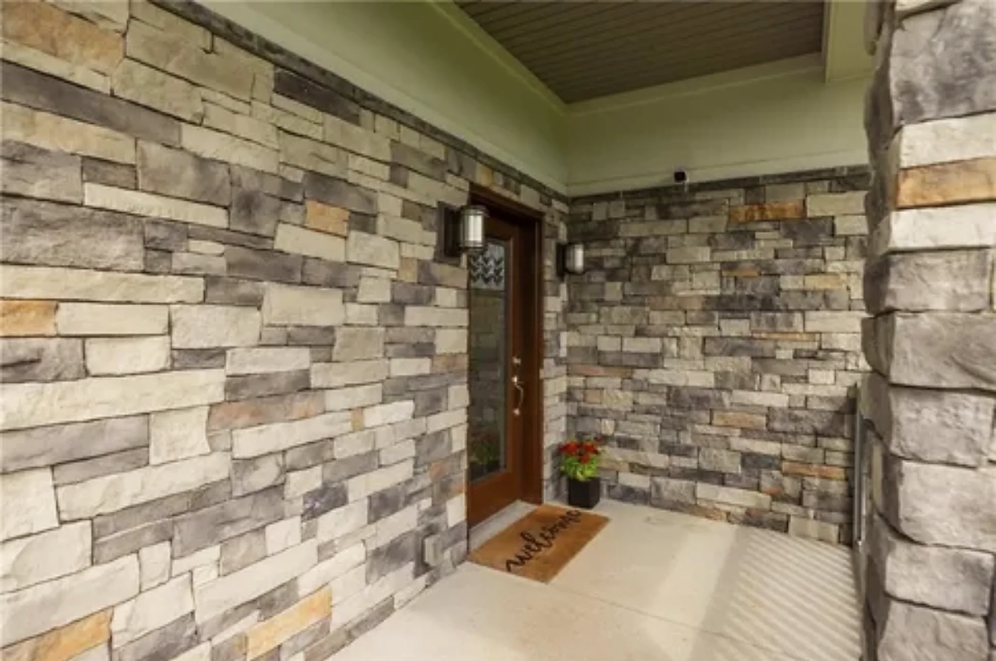 A covered entry porch faced in stacked gray stone, with a woodgrain front door and a glass insert.